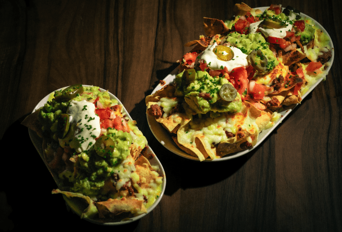 Nachos Gr. Tortas de maíz tostadas con carne picada de vacuno mayor, frijoles, jalapeños y queso fundido. Acompañado con guacamole, pico de gallo casero y crema agria gR.