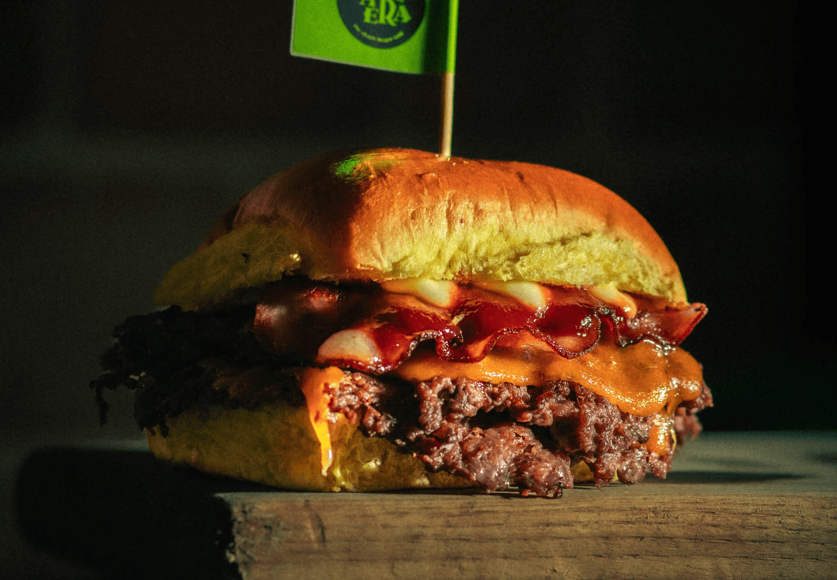 Paco de L. Cebolla cruda smasheada junto con la carne, doble queso cheddar, bacon crujiente y salsa BBQ Heinz en el pan superior y mahonesa Heinz en el inferior.